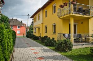 a yellow building with a balcony and a sidewalk at Bodó Park Apartment in Hévíz