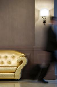 a person walking past a gold couch with a lamp at The Originals City, Hôtel Astoria Vatican, Lourdes (Inter-Hotel) in Lourdes