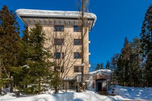 a building with snow on the ground next to trees at Wadano Forest Hotel & Apartments in Hakuba