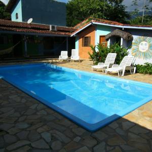 a blue swimming pool with chairs and a house at Pousada do Sidão in Ilhabela