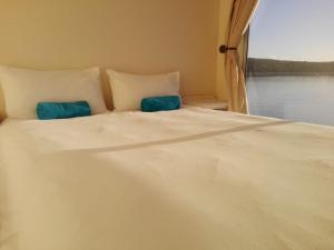 a white bed with two blue pillows and a window at Kraalbaai Lifestyle House Boats in Langebaan