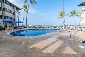 a swimming pool at the beach with palm trees and the ocean at Kona Reef Hawaii by Raintree in Kailua-Kona