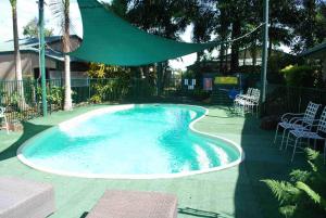 una piscina con ombrellone e sedie verdi di Rainforest Motel a Mission Beach