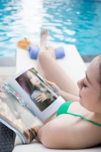 a woman reading a book next to a swimming pool at Muong Thanh Luxury Ca Mau Hotel in Cà Mau