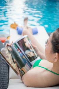een vrouw in bikini die een tijdschrift leest naast een zwembad bij Muong Thanh Luxury Ca Mau Hotel in Cà Mau
