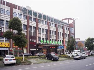 a large building with cars parked in front of it at GreenTree Inn Suzhou Kunshan Dongcheng Road International Exhibition Express Hotel in Penglang