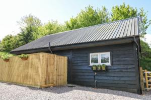 un pequeño cobertizo negro con una ventana y una valla en Woodpecker Lodge en High Ham