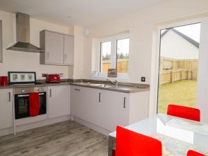 a kitchen with white cabinets and red chairs at 3 Osprey Drive in Boat of Garten