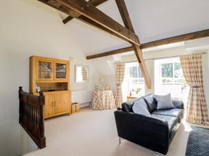 ein Wohnzimmer mit einer schwarzen Ledercouch und zwei Fenstern in der Unterkunft Carpenters Cottage in Cockermouth
