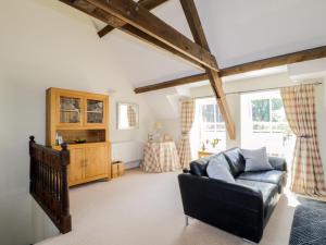 a living room with a black leather couch and two windows at Carpenters Cottage in Cockermouth