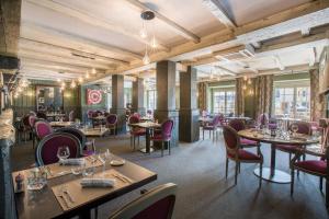 a restaurant with tables and chairs in a room with windows at Logis Hôtel Le Beaulieu in Beaulieu-sur-Dordogne