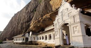 a man standing in front of a building next to a mountain at Sigiri Rangana Guesthouse in Sigiriya