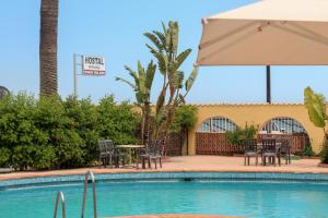 - une piscine avec des chaises, une table et un parasol dans l'établissement Hostal Esperanza, à Benajarafe