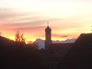 ein Gebäude mit einem Uhrturm bei Sonnenuntergang in der Unterkunft Alte Postvilla in Oberammergau