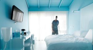 a man standing next to a bed in a blue room at Sesa Boutique Hotel & Restaurant - Small Luxury Hotels of The World in Kanali