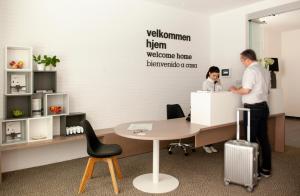 Due uomini in un ufficio con una scrivania e un uomo con una valigia di Eric Vökel Boutique Apartments - Hamburg Suites ad Amburgo