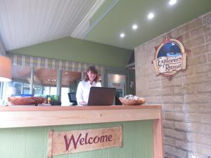 a woman standing behind a counter with a laptop at Explorers Retreat Matlock Bath in Matlock