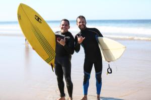 two men in wet suits standing on the beach with their surfboards at Natural Mystic Hostel in Costa da Caparica