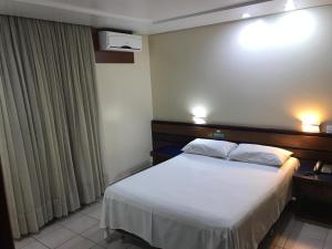 a hotel room with a bed with white sheets at Oft Plaza Oeste Hotel in Goiânia