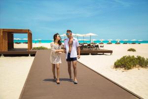 a man and a woman walking on a beach at Saadiyat Rotana Resort and Villas in Abu Dhabi