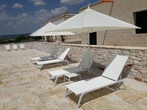 een rij witte stoelen en een paraplu bij Masseria La Gravina in Palagianello