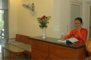 a woman sitting at a desk with a book at Ha Anh Hotel - Mui Ne in Mui Ne