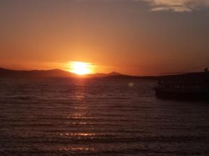 una puesta de sol sobre el agua con un barco en Plaza Studios, en Agia Anna de Naxos