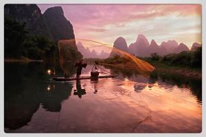a man is fishing on a boat in a river at Yangshuo Yunshe Mountain Guesthouse in Yangshuo