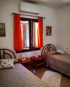 - une chambre avec 2 lits et une fenêtre avec des rideaux orange dans l'établissement Casa Duminicheddha, mare e relax in Gallura, à Bassacutena