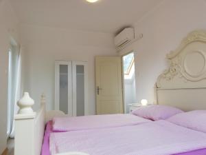 a white bedroom with a white bed with purple sheets at Fenyves Ferienhaus 1 **** in Balatonfenyves