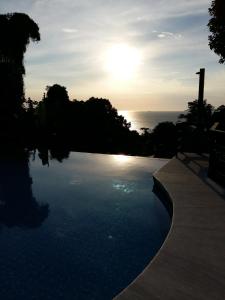 una piscina con puesta de sol sobre el océano en ILHABELA PRAIA DO CURRAL Condômino VilaBela da Princesa, en Ilhabela