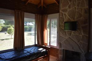 1 dormitorio con 2 ventanas y TV en una pared de piedra. en Cabañas Latitud 38.15 en Sierra de la Ventana