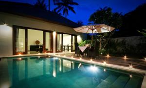 a swimming pool with an umbrella next to a house at Kebun Villas & Resort in Senggigi