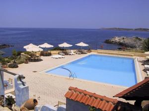 a large swimming pool next to the ocean with umbrellas at Giorgi's Blue Apartments in Kalathas