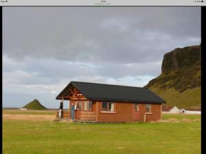 una piccola cabina in legno in un campo con una montagna di Vellir a Vík