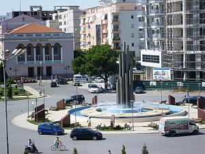 a city with a fountain in the middle of a parking lot at Hotel Kurtabeg in Shkodër
