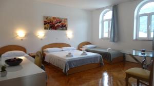 a room with two beds and a table and two windows at Guest House Mamut in Kaštela