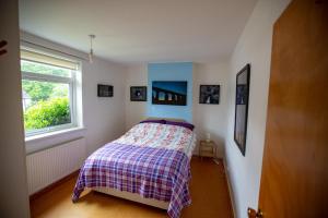 a bedroom with a bed with a plaid blanket and a window at Kelpies Cottage in Newton Stewart