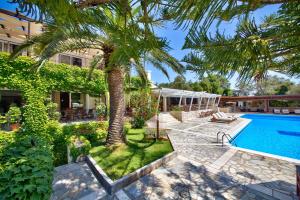 a palm tree in front of a house with a swimming pool at Paxos Club Resort & SPA in Gaios
