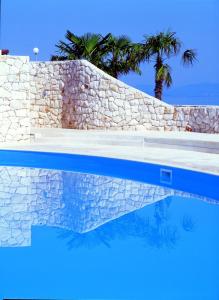 a swimming pool with a stone wall and palm trees at Apartments Marija in Postira