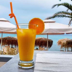 a glass of orange juice sitting on a table near the ocean at Mougre studios in Polychrono