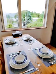 a table with plates and wine glasses and a window at Kashiwa House Furano in Furano