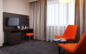 Habitación de hotel con silla naranja y TV en Demidov Plaza, en Nizhni Taguil