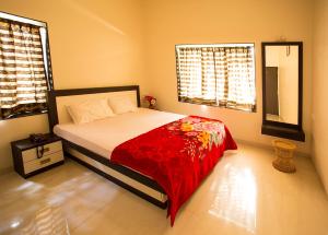um quarto com uma cama com um cobertor vermelho e 2 janelas em Aneesha Villa em Mahabaleshwar