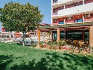 a building with tables and chairs and a tree at Topazio Vibe Beach Hotel & Apartments - Adults Friendly in Albufeira