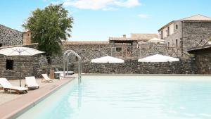 uma piscina com cadeiras e guarda-sóis ao lado de uma parede de pedra em Bosco Ciancio em Biancavilla