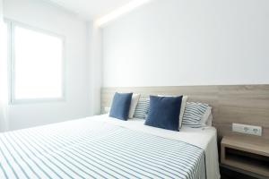 een witte slaapkamer met een bed met blauwe kussens bij Sea Breeze Apartments in Cala Millor