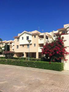 un grand bâtiment blanc avec des fleurs rouges devant lui dans l'établissement Pyla Village Resort F110 (Apartment near Larnaca), à Pýla