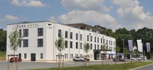 un gran edificio blanco con coches aparcados en un aparcamiento en i - PARK Hotel Klingholz en Reichenberg