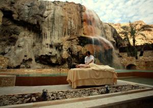 a woman sitting on a bed in front of a waterfall at Ma'in Hot Springs in Sowayma